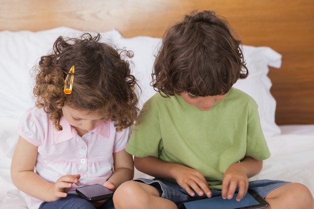 Bambini che utilizzano la tavoletta digitale e il cellulare a letto