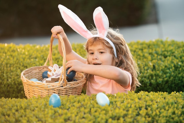 Bambini con le orecchie da coniglio durante la caccia alle uova di Pasqua in giardino bambino che raccoglie le uova concetto di caccia alle uova di Pasqua