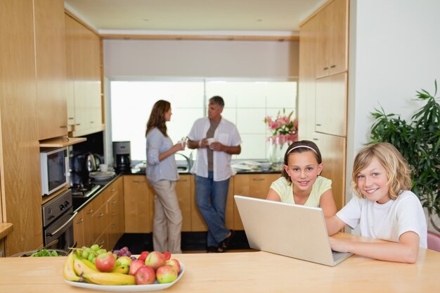 Bambini con notebook in cucina e genitori dietro di loro