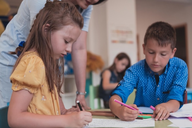 Bambini creativi durante una lezione d'arte in un asilo nido o in un'aula di scuola elementare che disegnano con un'insegnante femminile