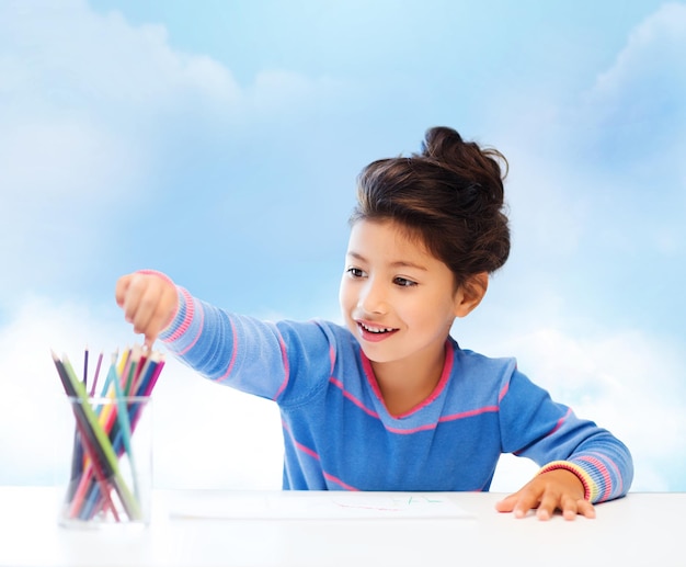 bambini, creatività e concetto di persone felici - bambina felice che disegna con matite colorate su sfondo blu cielo