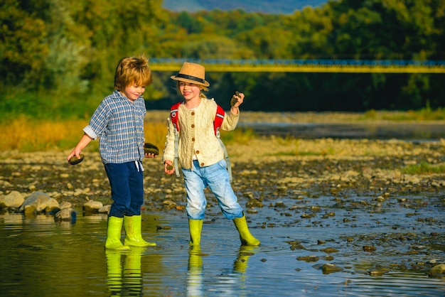 Bambini del fiume pietroso che lanciano sassi nel fiume dopo la scuola