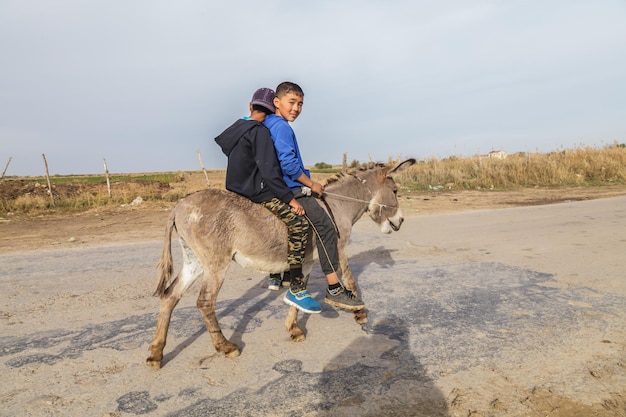 Bambini del villaggio che vivono nelle zone rurali del Kazakistan Bambini asiatici su un asino Kazakistan Shymkent 28 ottobre 2023