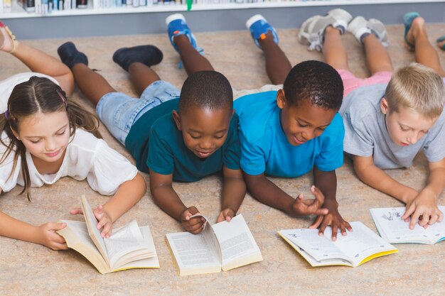 Bambini della scuola che si trovano sul libro di lettura del pavimento in biblioteca