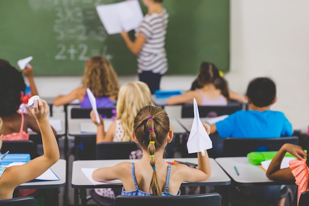 Bambini della scuola con gli aerei di carta in aula