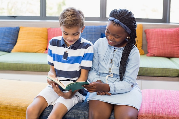 Bambini della scuola seduti insieme sul divano e leggendo un libro