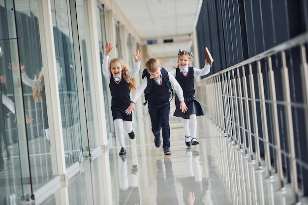 Bambini delle scuole attive in uniforme che corrono insieme nel corridoio Concezione dell'istruzione