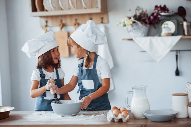 Bambini di famiglia in uniforme bianca da chef che preparano il cibo in cucina.