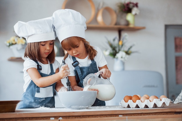 Bambini di famiglia in uniforme bianca da chef che preparano il cibo in cucina.