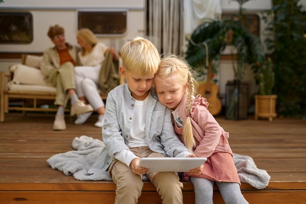 Bambini divertenti che usano il computer portatile al rimorchio, campeggio estivo. La famiglia con bambini viaggia in camper. Avventura in campeggio, stile di vita itinerante, vacanza in camper