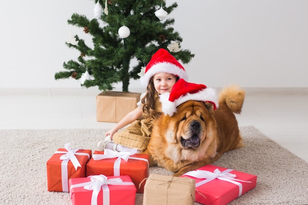 Bambini e concetto di animali domestici - Ragazza carina con cane da pasto seduto vicino all'albero di Natale. Buon Natale e Buone Feste.