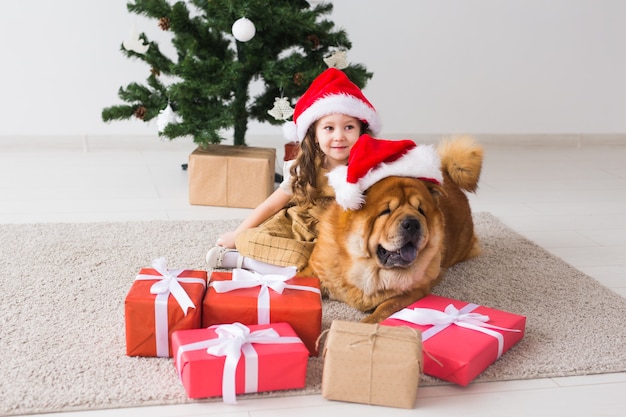 Bambini e concetto di animali domestici - Ragazza carina con cane da pasto seduto vicino all'albero di Natale. Buon Natale e Buone Feste.
