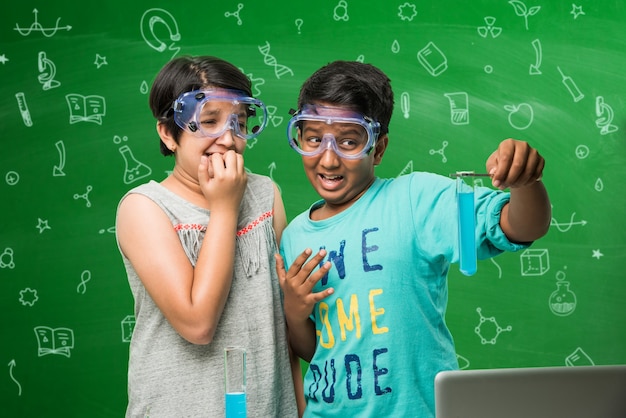 Bambini e concetto di scienza - carino studente indiano o scienziato che studia scienza o sperimenta con microscopio e prodotti chimici con diagrammi scarabocchi disegnati su lavagna verde