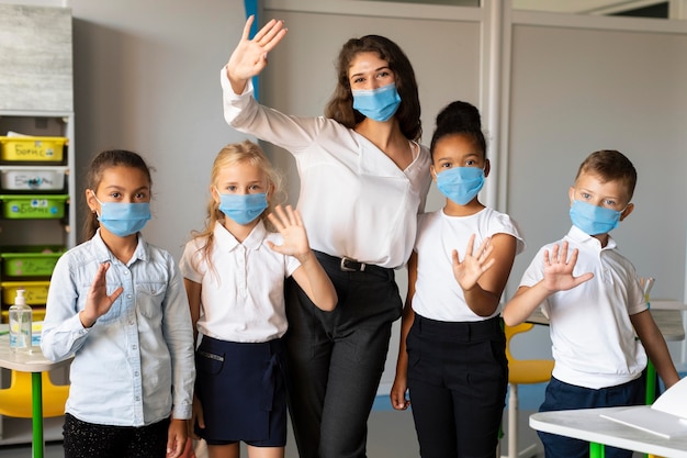 Bambini e insegnante in posa mentre indossa una maschera medica
