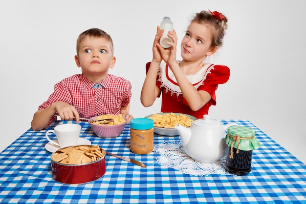 Bambini emotivi ragazzino e ragazza fratello e sorella che fanno colazione insieme contro lo studio grigio