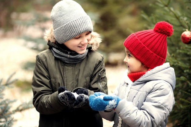 Bambini felici, bambina e ragazzo, che giocano all'aperto nella foresta invernale innevata e soffiano la neve.