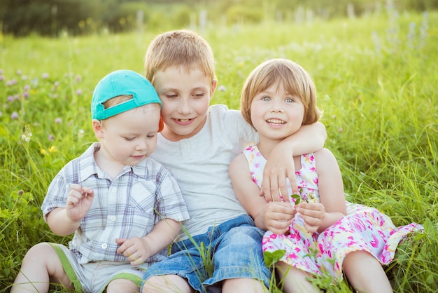 Bambini felici che abbracciano seduto sull'erba verde all'esterno