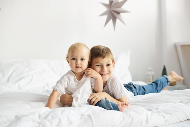 Bambini felici che giocano nella camera da letto bianca. Ragazzino e ragazza, fratello e sorella giocano sul letto.