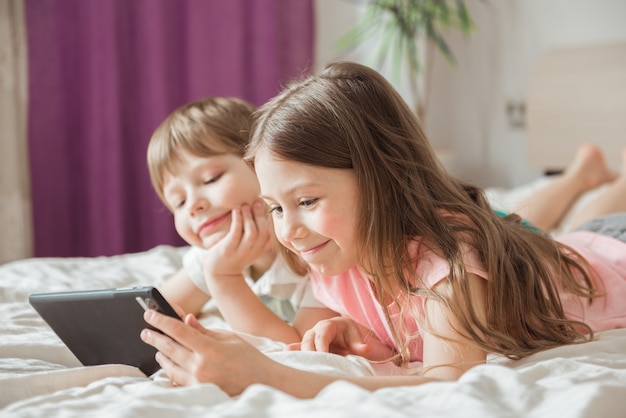 Bambini felici che guardano film online con ttablet digitale e sdraiati sul letto a casa