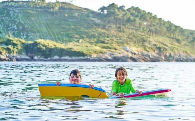 Bambini felici che guardano l'obbiettivo che giocano in mare con bodyboard. I bambini si divertono all'aperto. Concetto di vacanze estive e stile di vita sano.
