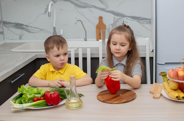 Bambini felici che si divertono con le verdure del cibo in cucina. Il concetto di dieta sana e stile di vita. Cibo vegano e stile di vita sano.