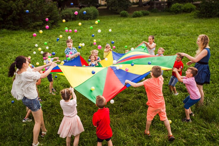 Bambini felici che sventolano il paracadute arcobaleno pieno di palle al prato verde
