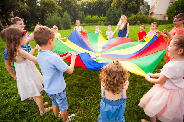 Bambini felici che tengono il paracadute durante il gioco divertente al parco estivo