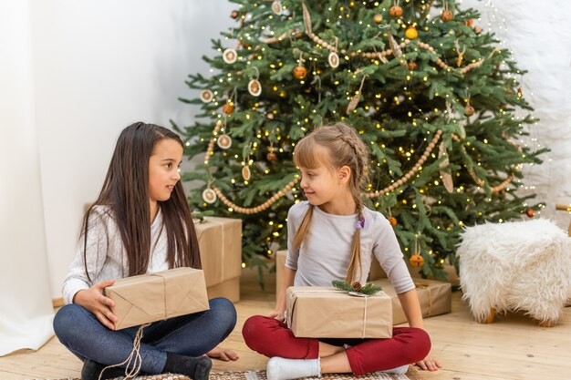 Bambini felici con doni. Gemelle, due sorelline, due ragazze simili che fanno regali. Vacanze e concetto di Natale.