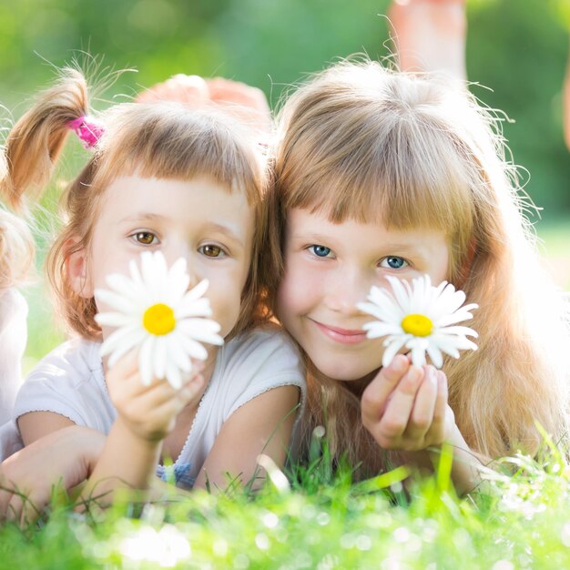 Bambini felici con fiori sdraiati sull'erba su sfondo verde primavera