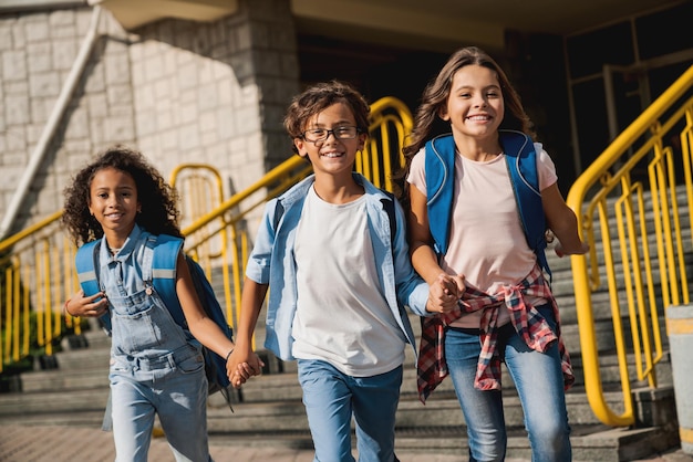 Bambini felici con gli zaini che camminano tenendosi per mano nel cortile della scuola