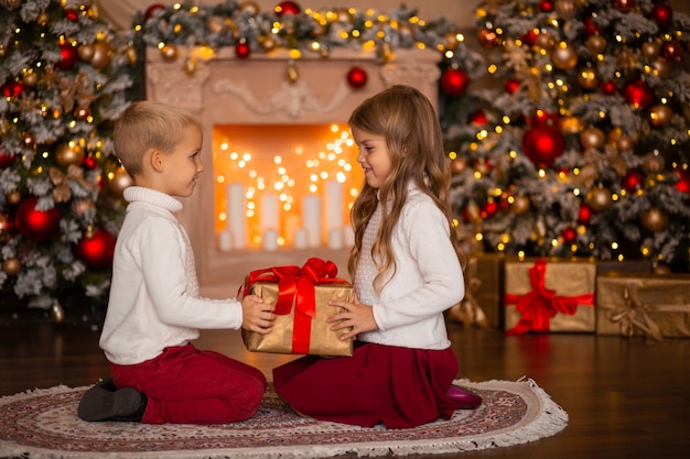 bambini felici con regalo a casa vicino all'albero di Natale e al camino