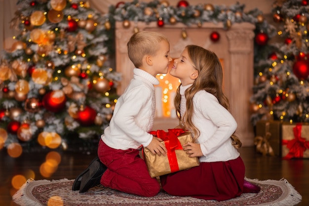 bambini felici con regalo a casa vicino all'albero di Natale e al camino