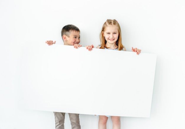 Bambini felici della ragazza e del ragazzo che tengono grande manifesto in bianco