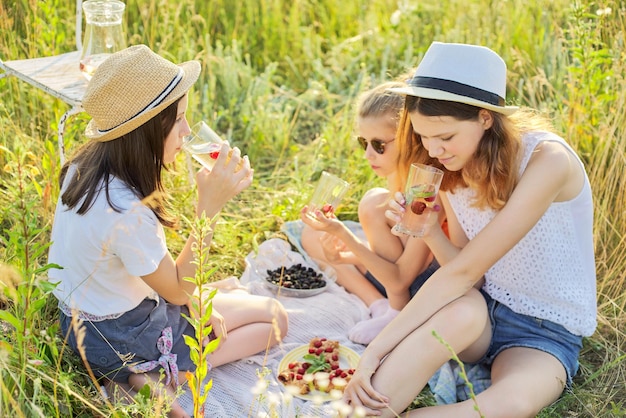 Bambini felici delle ragazze che mangiano torta di fragole e bevono tè con bacche di menta su picnic estate sfondo prato soleggiato Vacanza infanzia divertente concetto estivo