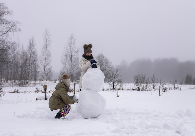 Bambini felici fanno un pupazzo di neve in un campo innevato in campagna.