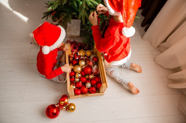 bambini felici in pigiama rosso stanno decorando un albero di Natale nel concetto di inverno del soggiorno