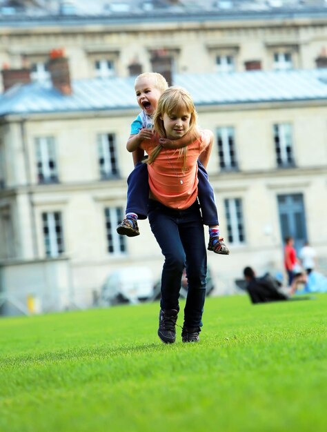 Bambini felici, scolaretta e suo fratellino, che giocano nel parco cittadino, correndo insieme sulle spalle