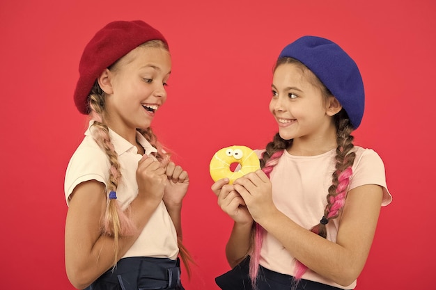 Bambini grandi fan di ciambelle al forno Condividi dolce ciambella Ragazze con cappelli berretto tengono ciambella smaltata sfondo rosso Bambini ragazze giocose pronte a mangiare ciambella Amicizia e generosità Negozio di dolci e concetto di panetteria