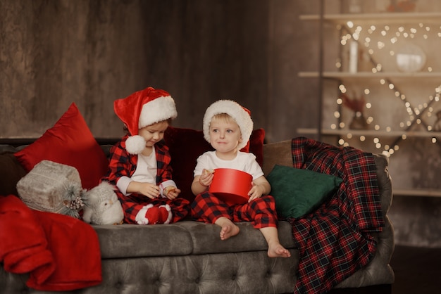 Bambini in cappelli di Babbo Natale su una grande sedia accogliente nel soggiorno