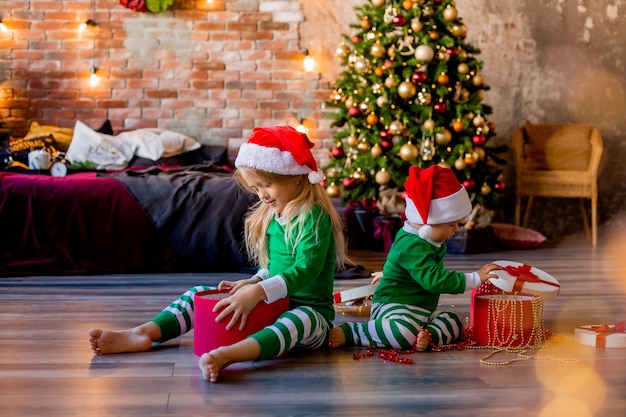 bambini in pigiama e cappelli natalizi disfano i regali di Natale