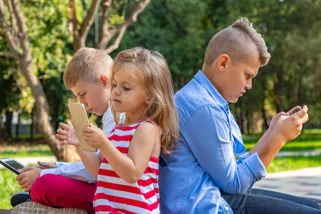 Bambini indaffarati che guardano i loro telefoni mandando sms e giocando seduti fuori