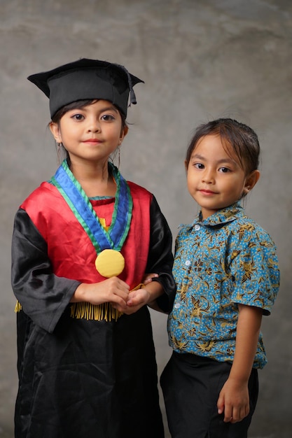 Bambini indonesiani che indossano un abito in piedi e sorridono alla telecamera Diploma di scuola materna