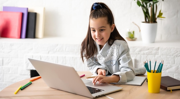 bambini, istruzione e concetto di apprendimento a distanza - piccola studentessa con computer portatile a casa