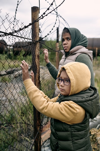 Bambini mediorientali tristi persi in piedi davanti al filo spinato e in attesa dei genitori