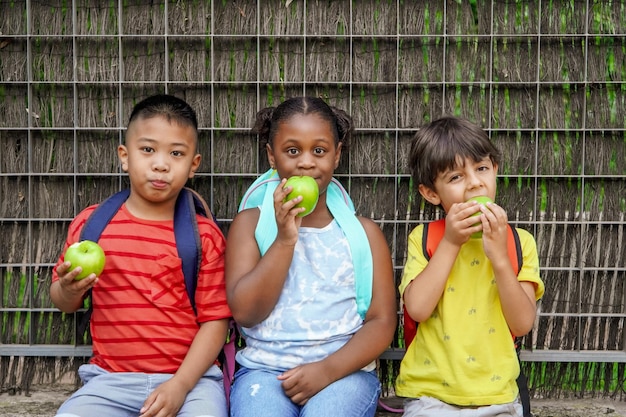 Bambini multietnici con zaini che mangiano mele all'ingresso della scuola