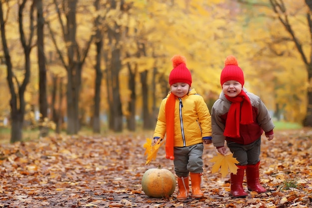 Bambini nel parco autunnale con la zucca intorno alle foglie d'autunno