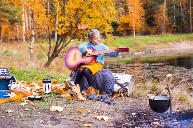 bambini nella foresta di autunno su un picnic grigliano salsicce e suonano la chitarra