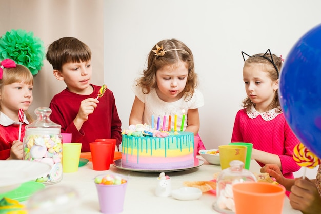 Bambini piccoli che festeggiano il compleanno. La ragazza esprime un desiderio prima di soffiare le candeline sulla torta