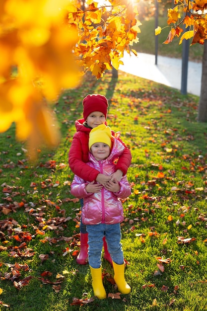 Bambini piccoli fratello e sorella in stivali di gomma e vestiti luminosi nel parco autunnale