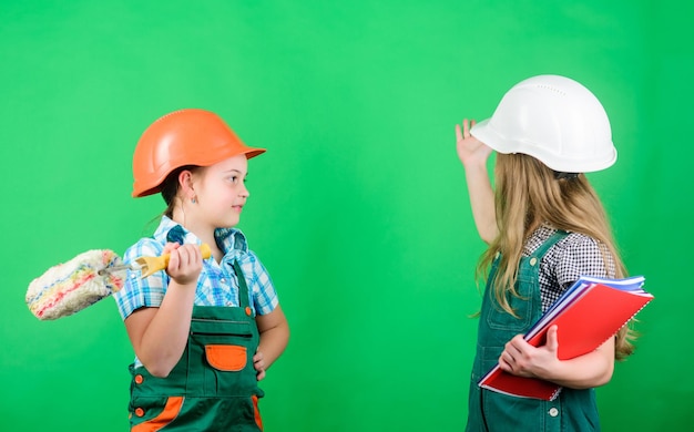 Bambini piccoli in casco con tablet e rullo Labor Day 1 maggio progetto scolastico Foreman Riparazione processo di lavoro bambine che riparano insieme in officina processo di lavoro processo di lavoro in azione